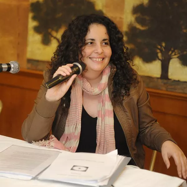 Η Διονυσία Κλανερτατζή κρατώντας μικρόφωνο σε αίθουσα συνέντευξης.